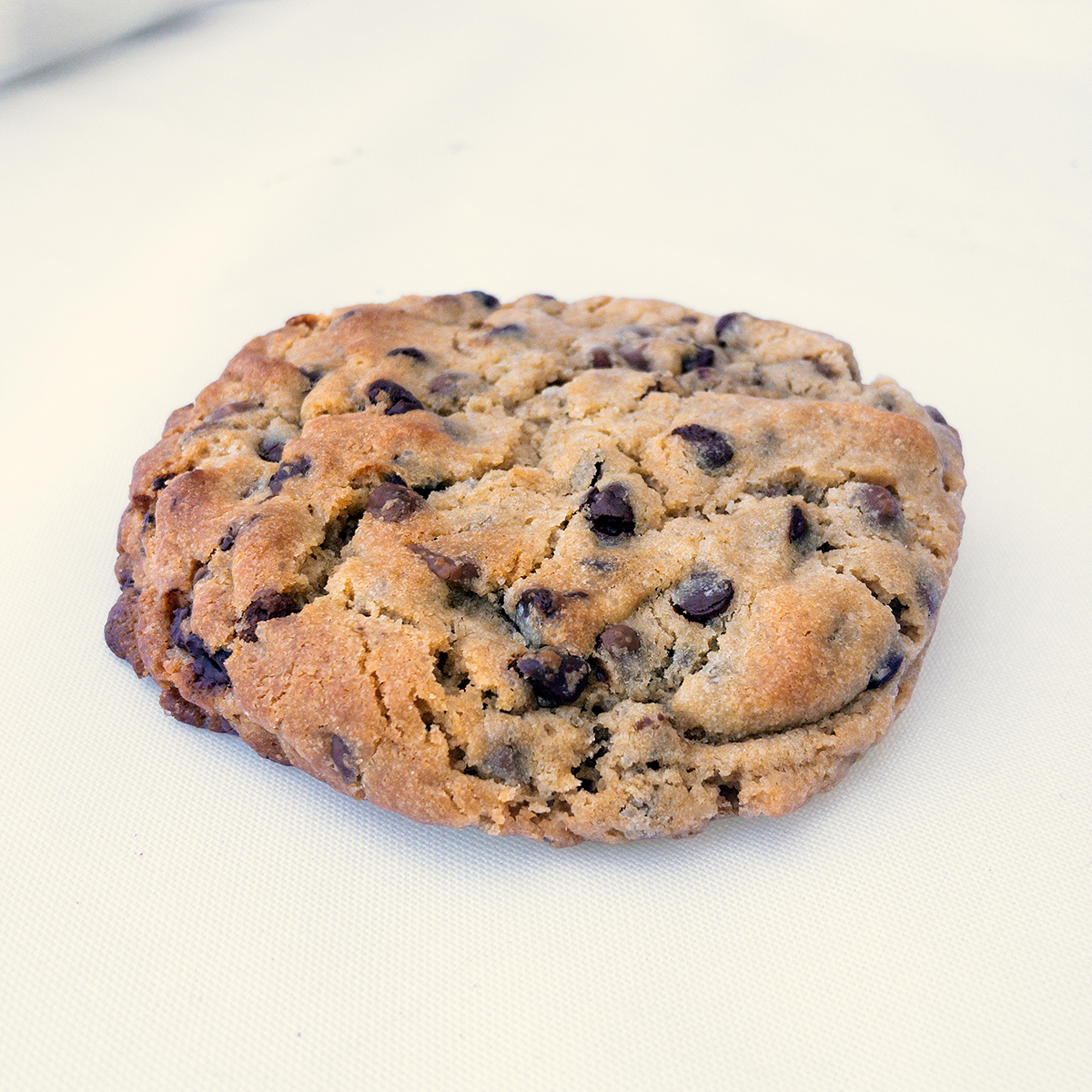 Cookie artesanal Milalevain con pepitas de chocolate, dorada y crujiente sobre superficie blanca